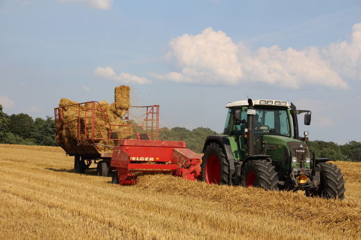 Traktor mit Ballenpresse auf Strohfeld